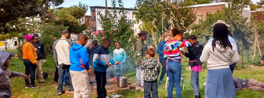 A group of adults and children gathers in an urban orchard surrounding 