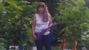 Growing figs AND electric violins! Jeanette in her garden holding a solid-body violin she created. 